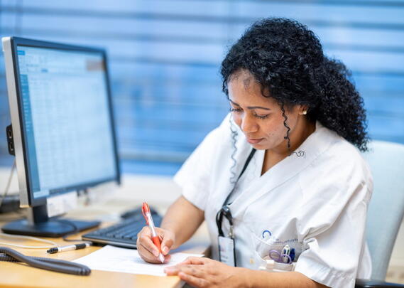 En sykepleier foran en pc noterer på et ark 