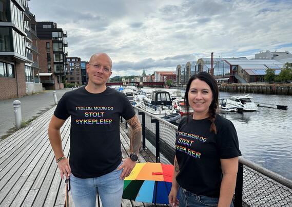 Fylkesleder i Trøndelag Kenneth Sandmo Grip og fylkesnestleder Randi Wågheim i sorte t-skjorter med regnbuefarget tekst "tydelig, modig stolt sykepleier"