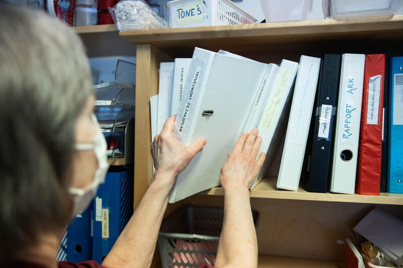 Illustrasjonsfoto: sykehjem, sykepleier tar ut en perm fra kontorhylle