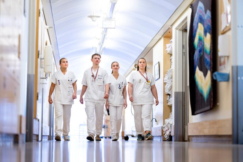 Fire sykepleiere i uniform går bortover en korridor med ansiktet mot kamera.
